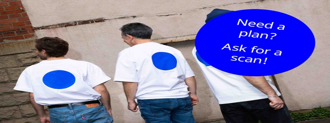 punktWOLKE: Team – Ansicht von hinten Drei Architekten und Ingenieure in weißem T-Shirt mit leuchtend blauem Punkt und blauer Jeans stehen vor einer Wand.